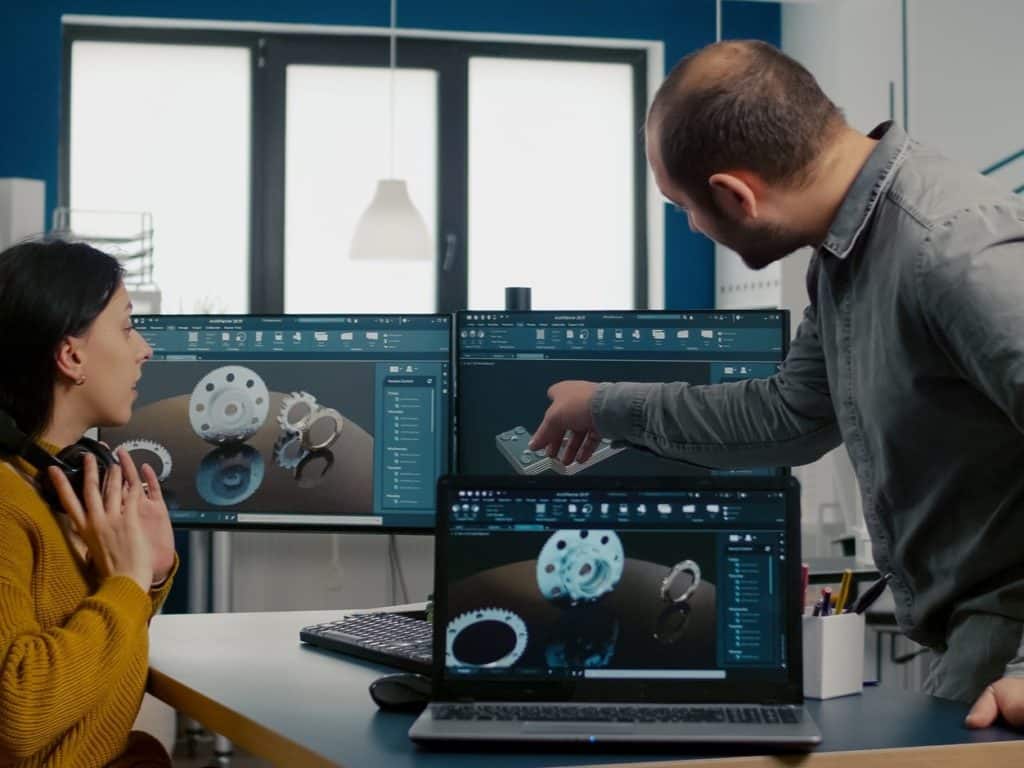 Dos ingenieros revisando modelos CAD 3D de engranajes y componentes mecánicos en software industrial de diseño
