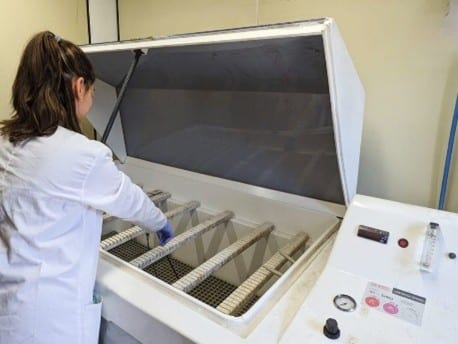 Accelerated corrosion testing to optimize laser marking in industrial materials Laboratory technician placing samples in a salt spray chamber to perform an accelerated corrosion test and evaluate material resistance.